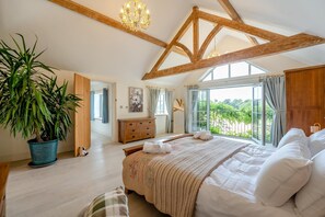 Ein Schlafzimmer mit einem großen Bett, Holzbalken, einem Blumentopf und Blick aus dem Fenster.