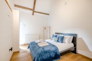 Ein Schlafzimmer mit Bett, Heizkörper, Holzbalken und einem Fenster.