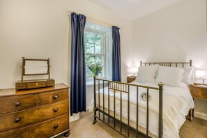 Een slaapkamer met een bed, een houten dressoir en een raam met gordijnen.