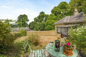 Ein Garten mit Holzzaun, einem Tisch und einem Stuhl sowie ein Haus mit Schornstein.