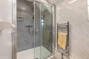 Un bany modern amb dutxa tancada amb vidre, una banyera blanca i un suport de tovalloles amb una tovallola groga.