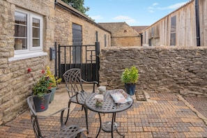 A courtyard with stone walls, a metal table, chairs, and potted plants. - 4 Bed in Ebberston (oc-h45939) (Ebberston)