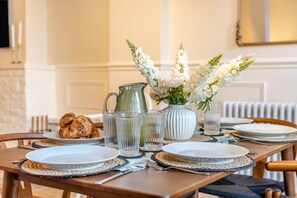 Et spisebord dækket med tallerkener, glas, kande og en vase med blomster.