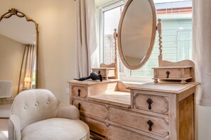 Ein Schlafzimmer mit Schminktisch, Spiegel, Stuhl und einem Fenster mit Vorhängen.