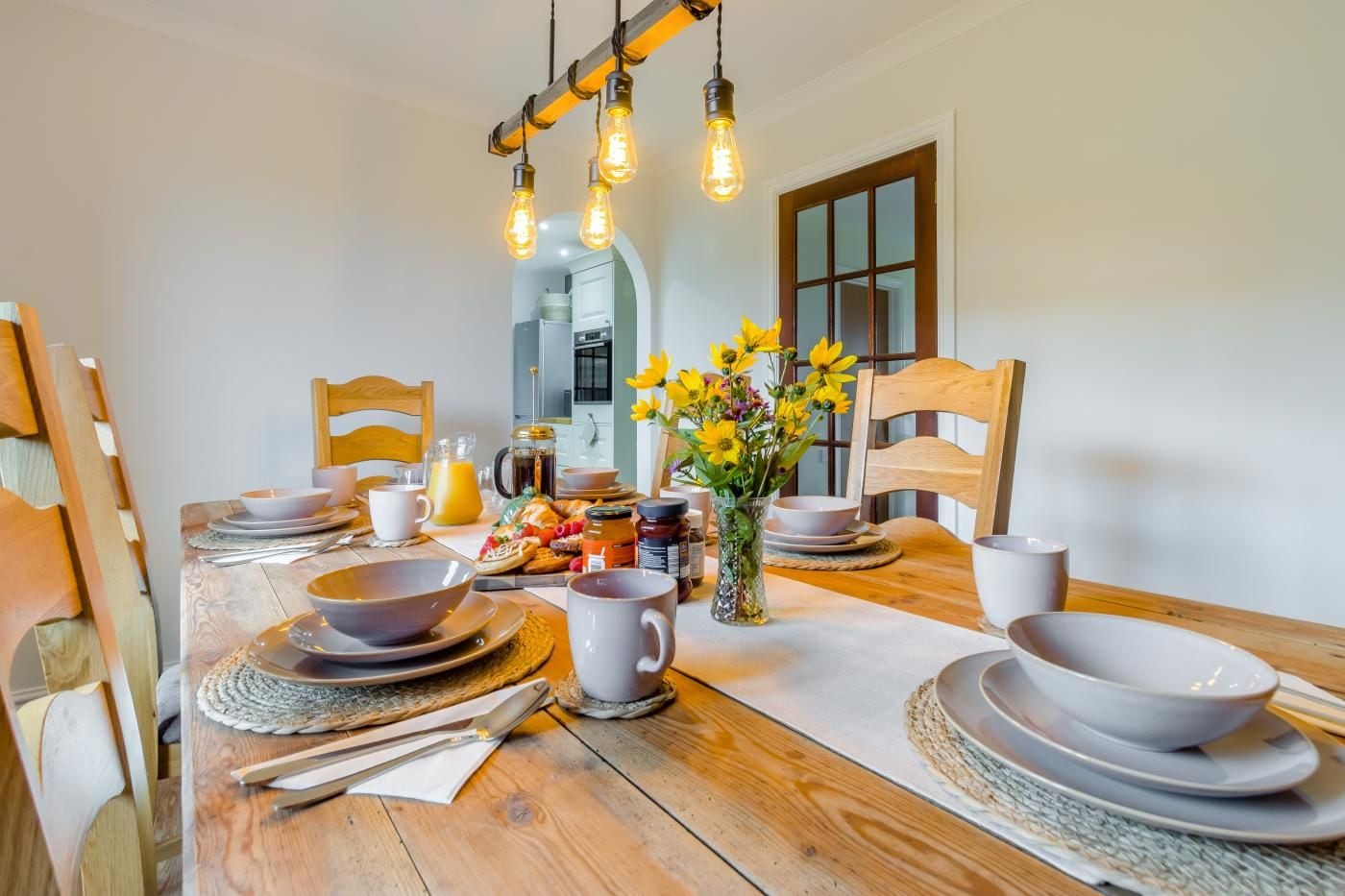 A dining area with a wooden table set for breakfast, including plates, bowls, and a pitcher of orange juice.