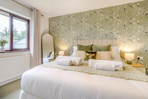Ein ordentlich bezogenes Bett mit Kissen und Decke, ein Nachttisch mit Lampe sowie ein Fenster mit Vorhängen.