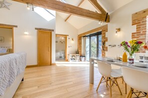 Ein modernes Interieur mit Holzboden, einer Essecke mit weißen Stühlen, einer Küche mit Backsteinwänden und einem großen Fenster.