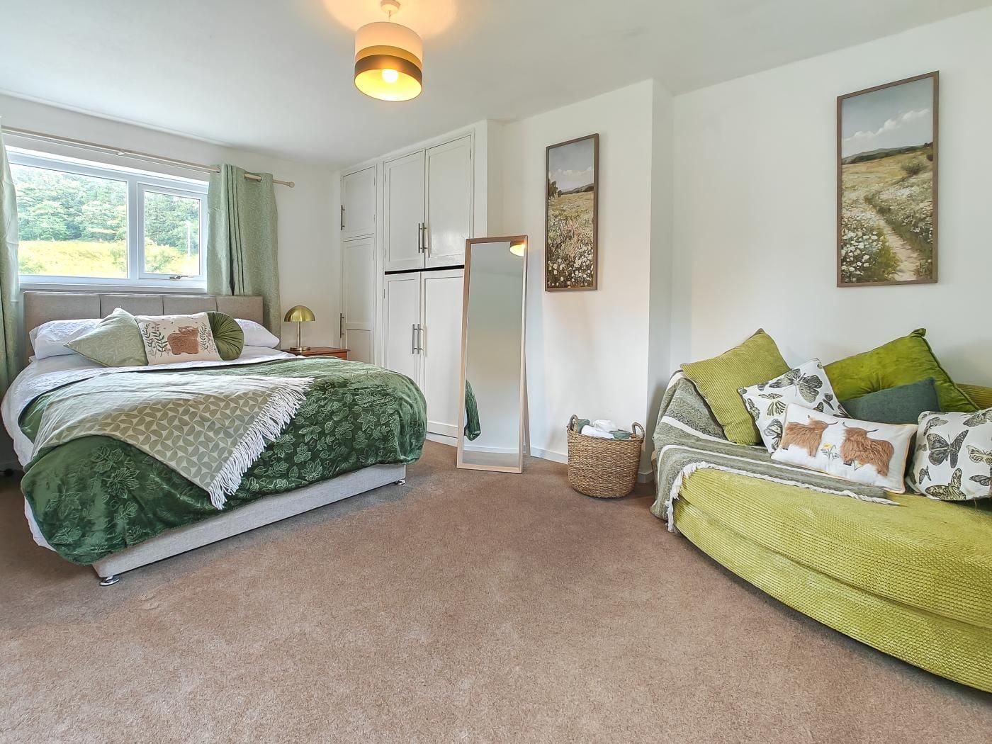 A bedroom with a bed, a sofa, a wardrobe, a mirror, and a window.