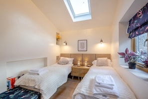 A bedroom with two beds, a skylight, bedside lamps, a framed picture, and a window with a plant. - 5 Bed in Cerrigydrudion (oc-c45945) (Cerrigydrudion)