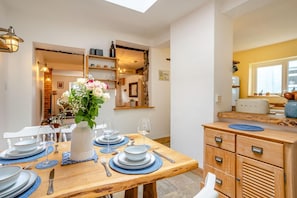 A dining area with a wooden table set for four, a vase with flowers, and a kitchen area with a toaster and cabinets. - 2 Bed in Mumbles (oc-c45992) (The Mumbles)