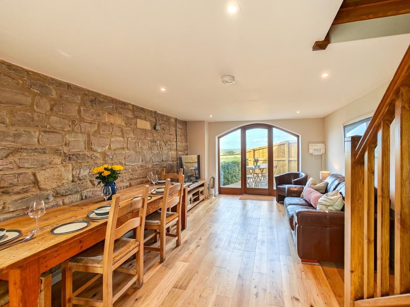 A spacious dining area with a stone wall, wooden furniture, and a view to a garden.