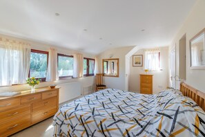 Une chambre à coucher avec un lit, une commode, une chaise et une fenêtre avec des rideaux.