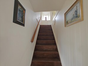 Eine Holztreppe mit weißen Wänden und einem Fenster am Obergeschoss.