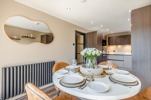 A modern dining area with a round table set for four, a vase of white flowers, and a kitchen in the background. - 2 Bed in Greenhow Hill (oc-h46025) (Greenhow Hill)