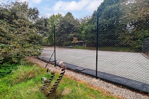 Ein eingezäunter Tennisplatz mit einer Bank und einer Metallskulptur im Vordergrund.