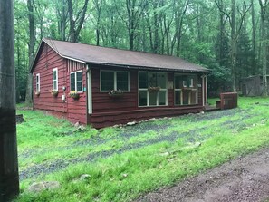A red wooden cabin with a sloped roof, large windows, and flower baskets on the windowsills. - Wonderful 3-bedroom house with AC in charming Lake Harmony (Lake Harmony)
