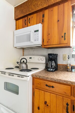 A kitchen with white appliances, wooden cabinets, a kettle, a coffee maker, and a tiled backsplash. - Wonderful 3-bedroom house with AC in charming Lake Harmony (Lake Harmony)