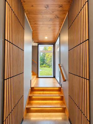 Un intérieur moderne avec un escalier en bois menant à une pièce lumineuse offrant une vue sur la verdure environnante.