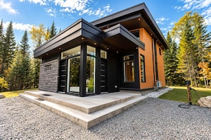 A modern two-story house with a stone facade, large glass windows, and a gravel driveway. - Pool, Spa & Nature - Chalet Volcano (Notre-Dame-de-la-Merci)
