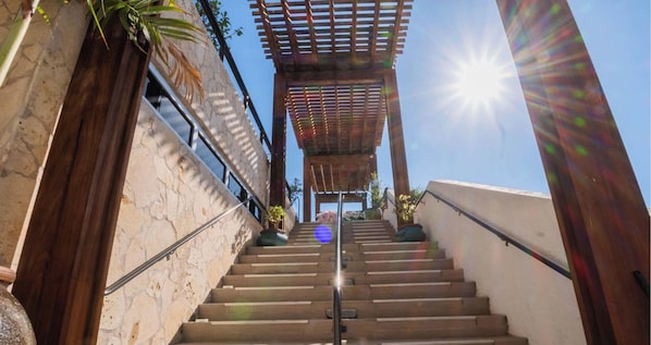 A staircase leading to a covered area with a pergola, surrounded by stone walls and potted plants. - Modern Waterway Apt 2BR Beachwalk Resort (Hallandale Beach)