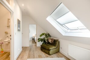 Ein modernes Schlafzimmer im Loft-Stil mit Dachfenster, Holzboden, einem grünen Sofa und Blick in das angrenzende Schlafzimmer.