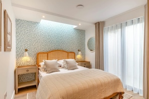 Ein modernes Schlafzimmer mit einem großen Bett, zwei Nachttischen, einer Wandleuchte und einem Fenster mit Vorhängen.