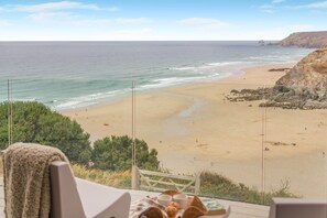 Blick auf einen Sandstrand und den Ozean vom Balkon aus, mit Tisch und Stühlen.