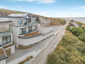 A modern coastal building with a curved facade, large windows, and a flat roof. - 4 Bed in Porthtowan (oc-m45962) (Porthtowan)