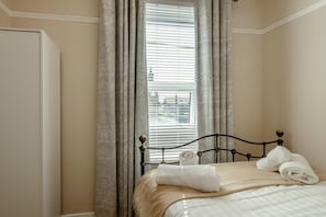 Ein Schlafzimmer mit einem Bett, Vorhängen und einem Fenster mit Jalousien.