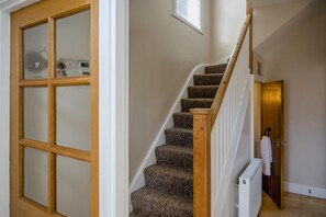 Eine Treppe mit Teppichstufen und Holzhandläufen führt zu einem Raum, in dem ein weißer Heizkörper und eine Tür mit einem aufgehängten Handtuch zu sehen sind.