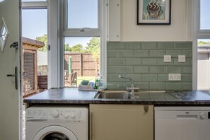 A kitchen with a washing machine, a sink, and a window overlooking a backyard. - 3 Bed in Seahouses (oc-f46039) (Seahouses)