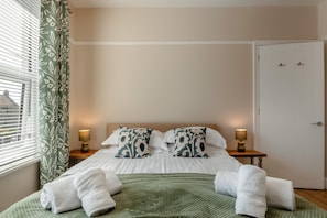 Ein Schlafzimmer mit einem Bett, zwei Nachttischlampen, einer grünen Decke und einer weißen Tür.
