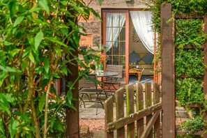 A wooden gate leading to a patio with a table and chairs, a sofa, and a window with curtains. - 2 Bed in Berwick-upon-Tweed (oc-s46040) (Kyloe)
