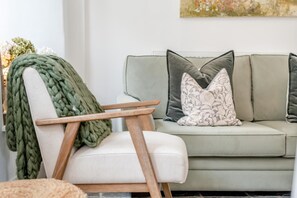 A modern living room with a light-colored sofa, a wooden chair with a green throw blanket, and decorative pillows. - 1 Bed in Trevelmond (oc-46051) (Trevelmond)