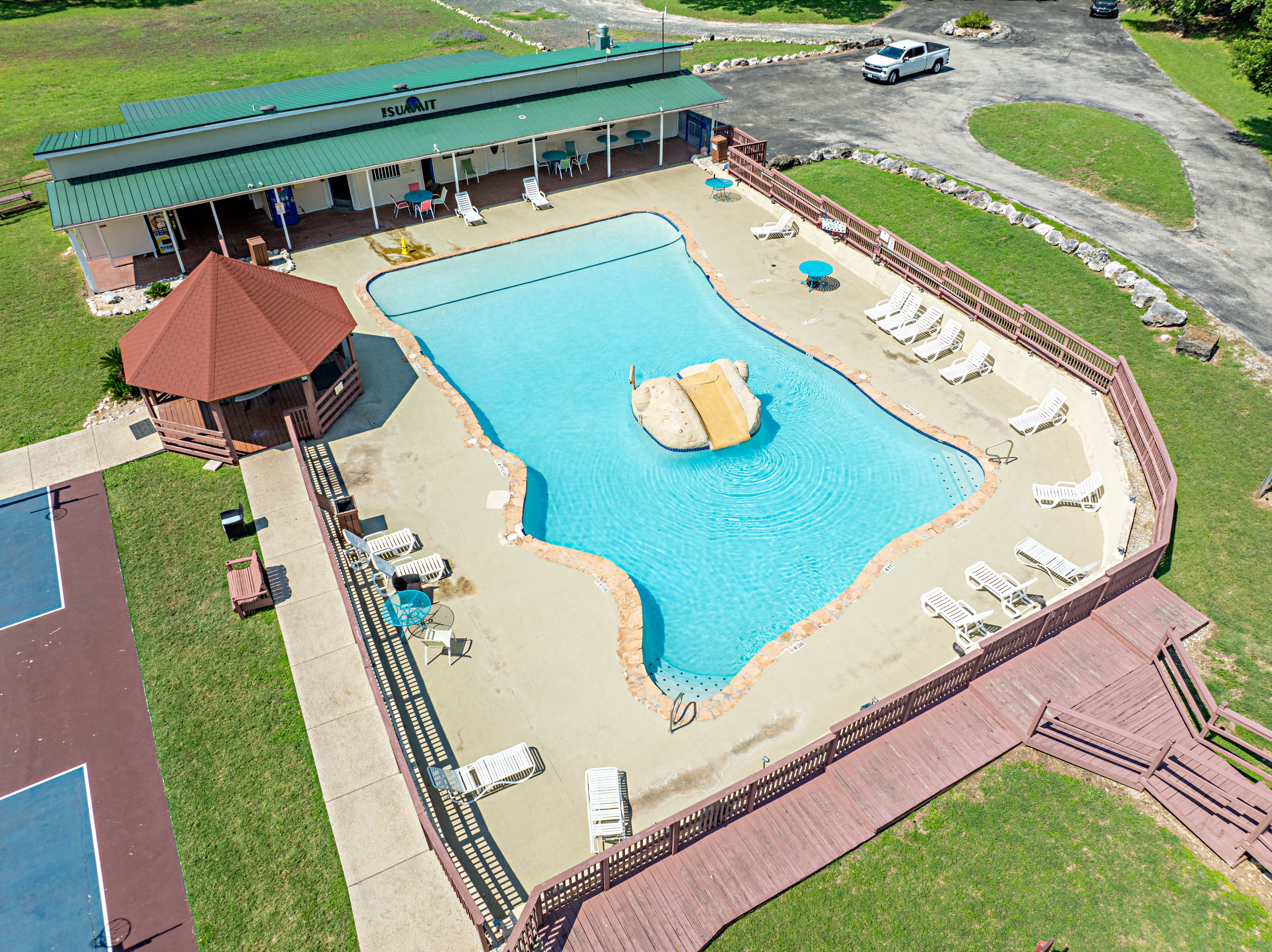 A swimming pool with lounge chairs, a covered seating area, and a building with a green roof.