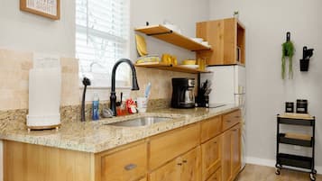A kitchen with wooden cabinets, a granite countertop, a coffee maker, and a small plant on the wall.