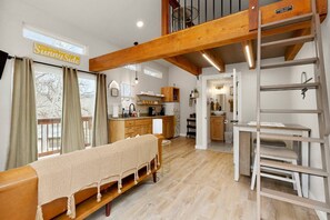 A cozy room with a bed, a wooden bench, a kitchen area, and a loft with a ladder.