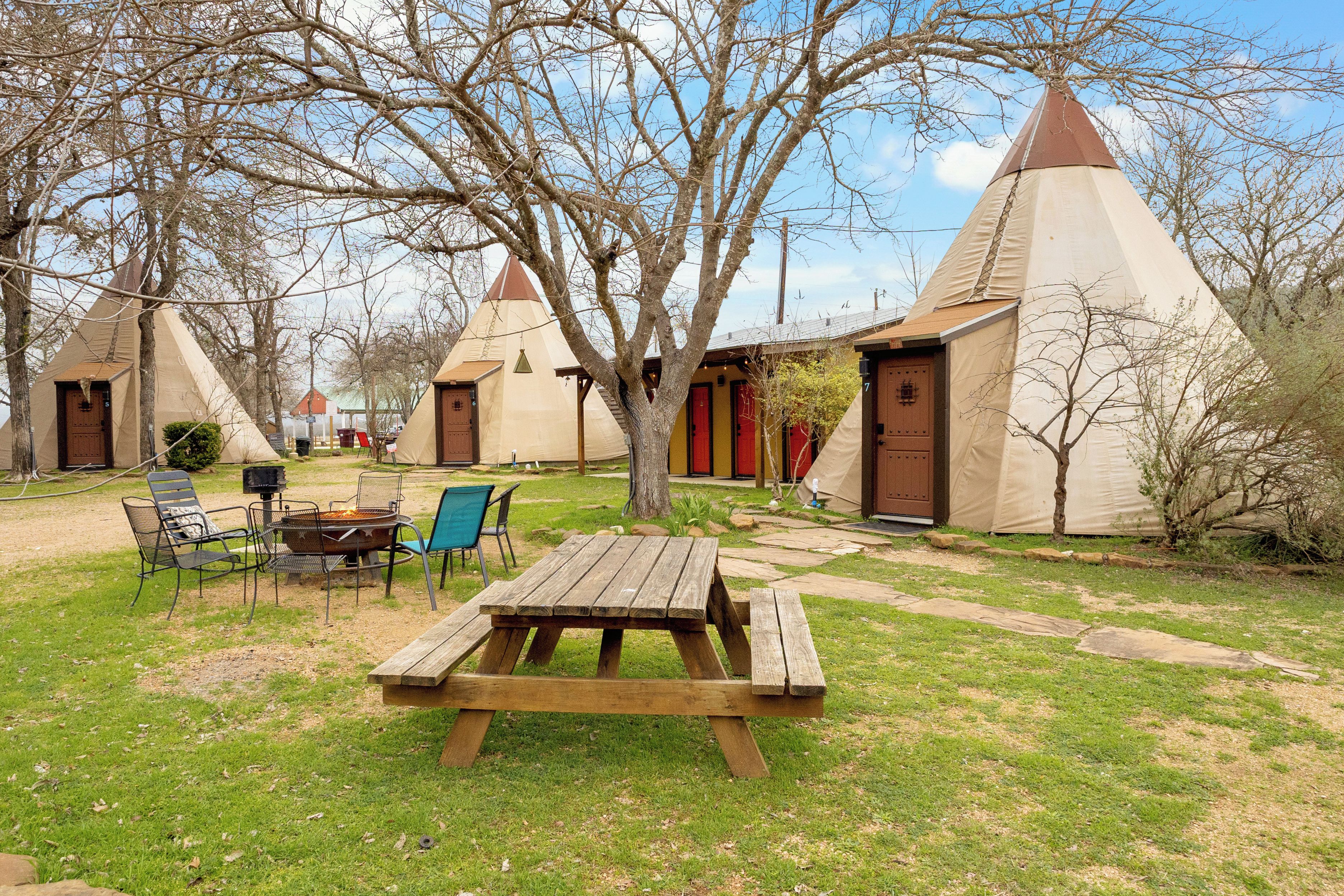 A campsite with a wooden picnic table, chairs, and a fire pit.