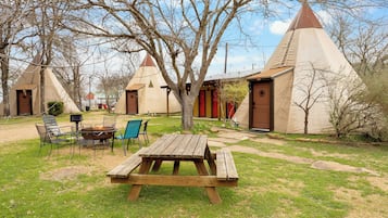 A campsite with a wooden picnic table, chairs, and a fire pit.