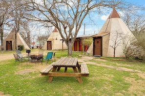 A campsite with a wooden picnic table, chairs, and a fire pit. - Summit Vacation and RV Resort (New Braunfels)