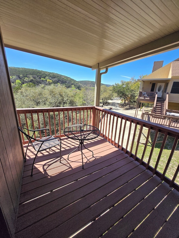 Une terrasse en bois avec une table et des chaises en métal, donnant sur un paysage vallonné.