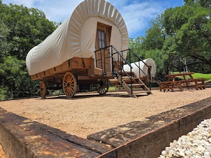 A covered wagon with wooden wheels and a ramp leading to the entrance.