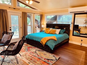 A bedroom with a large bed, a ceiling fan, and a view of the outdoors through the windows.