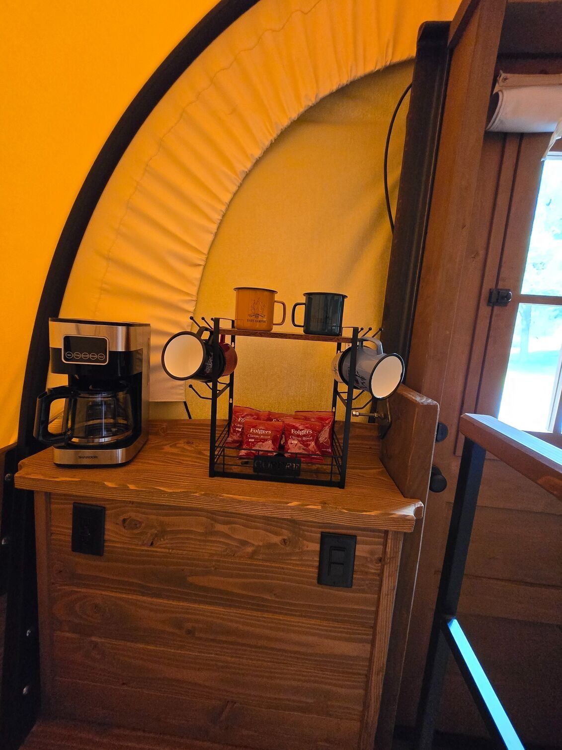 A kitchen area with a coffee maker, a mug rack, and a bag of coffee pods.