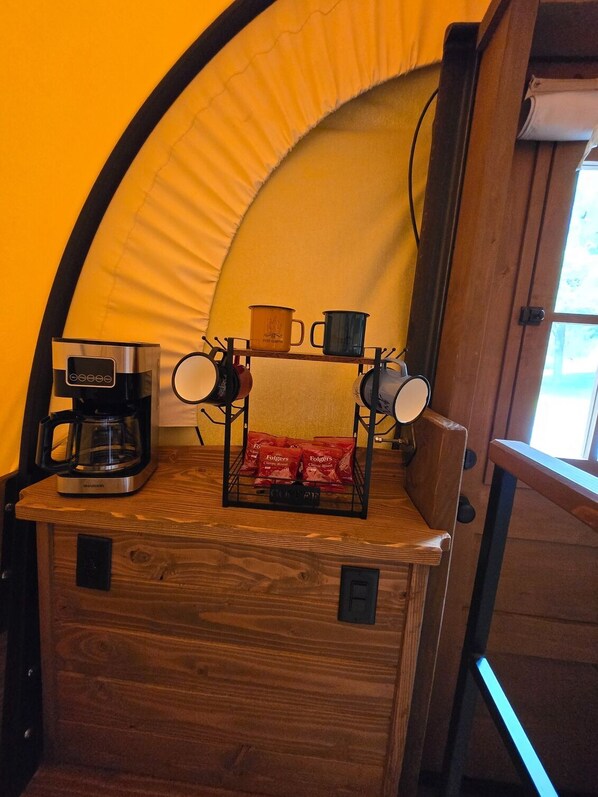 A kitchen area with a coffee maker, a mug rack, and a bag of coffee pods.