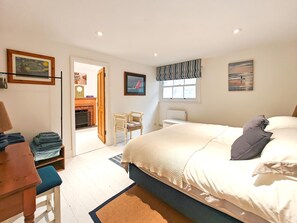 Un dormitorio con cama, escritorio, silla, chimenea y obras de arte en las paredes.