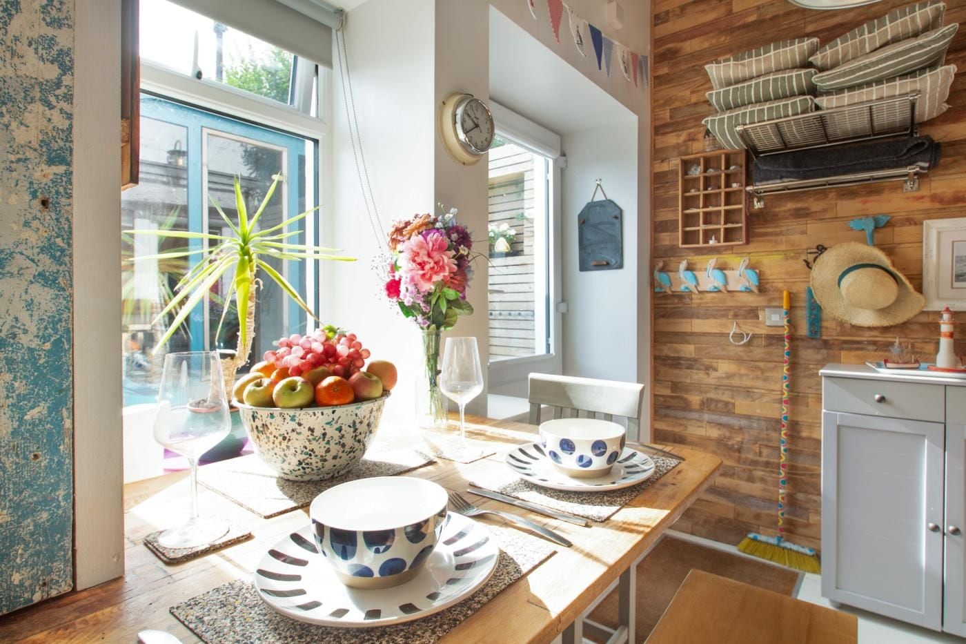 A dining area with a wooden table, a bowl of fruit, and a vase of flowers.