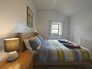 Ein Schlafzimmer mit einem Bett, einem Nachttisch, einer Lampe, einem Fenster und einer Heizung.