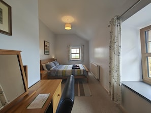 Quarto com cama, escrivaninha, cadeira, janela com cortinas e radiador.