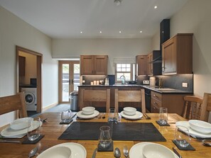 Une cuisine moderne avec des meubles en bois, un îlot central et un coin repas aménagé pour quatre personnes, comprenant une table, des chaises et de la vaisselle.